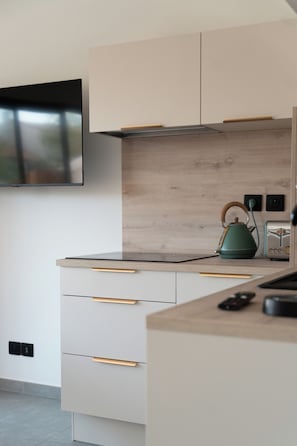 A modern kitchen with a flat-screen TV mounted on the wall, wooden cabinets, a countertop with a kettle, and a toaster. - Studio Dunes with a small garden (Mauguio)