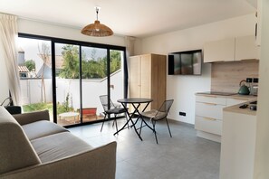 A modern kitchen with a TV, a dining table with chairs, and a sofa. - Studio Dunes with a small garden (Mauguio)