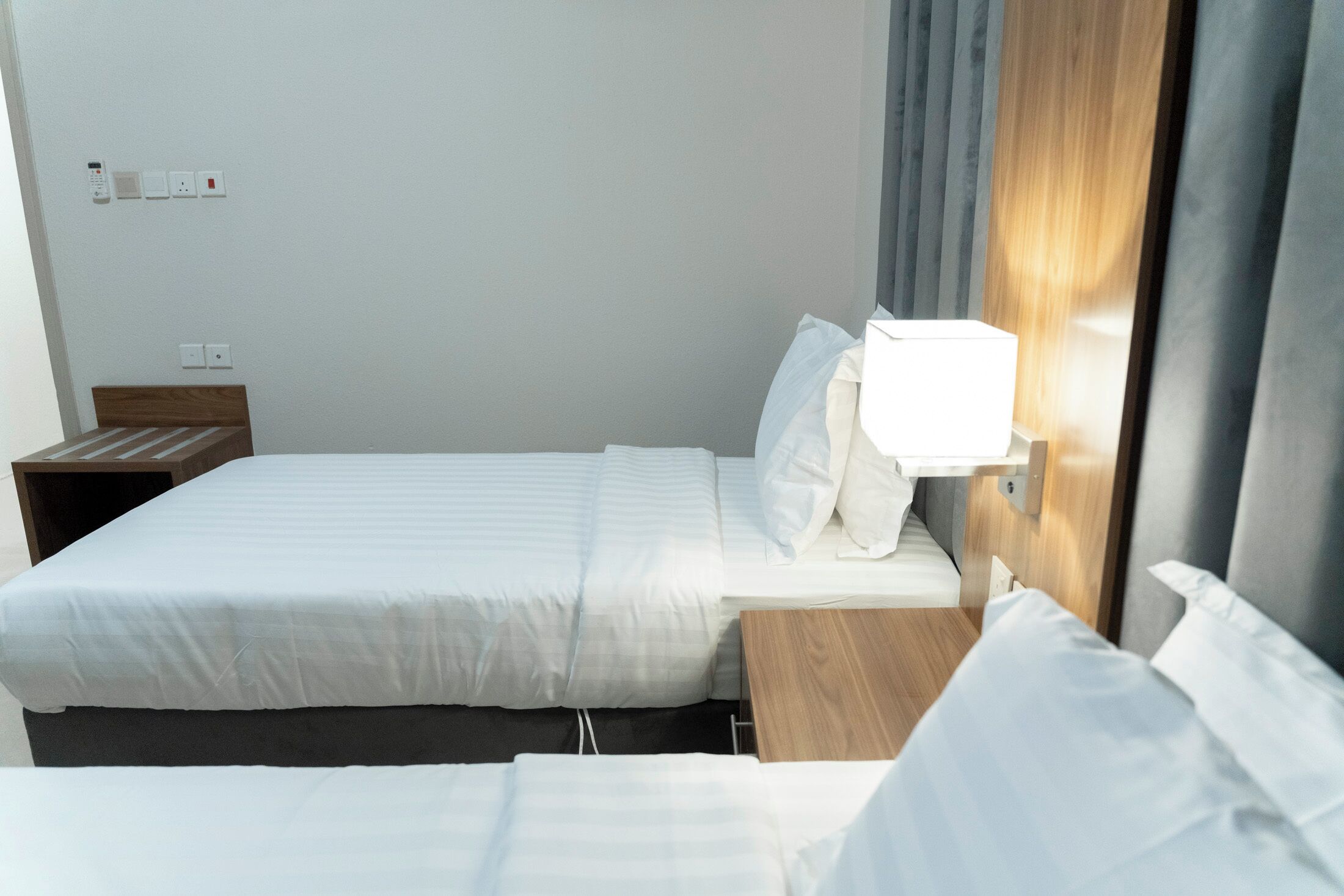 A hotel room with a single bed, bedside table, and a wall-mounted light.