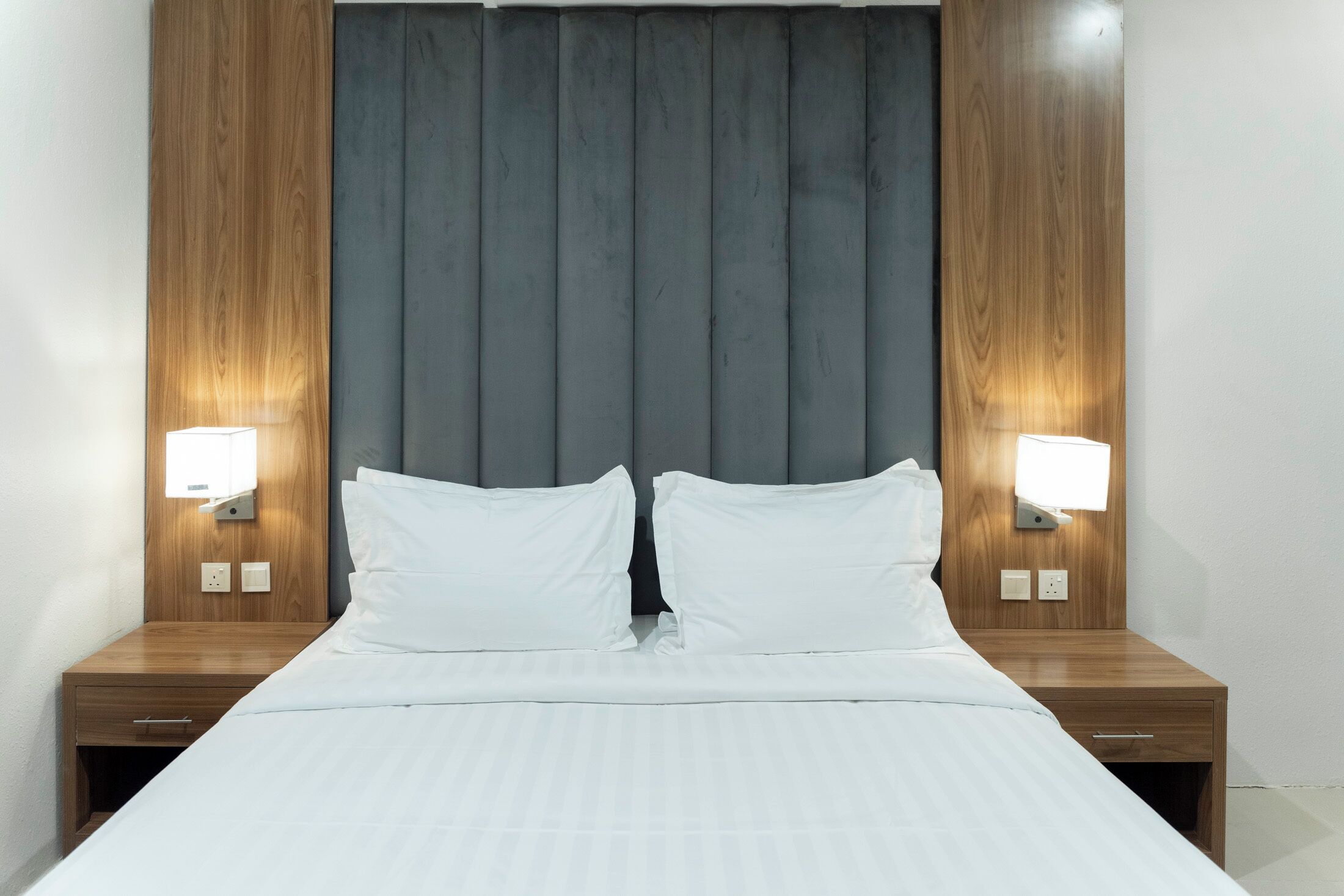 A hotel room with a large bed, two bedside tables, and two wall-mounted lamps.