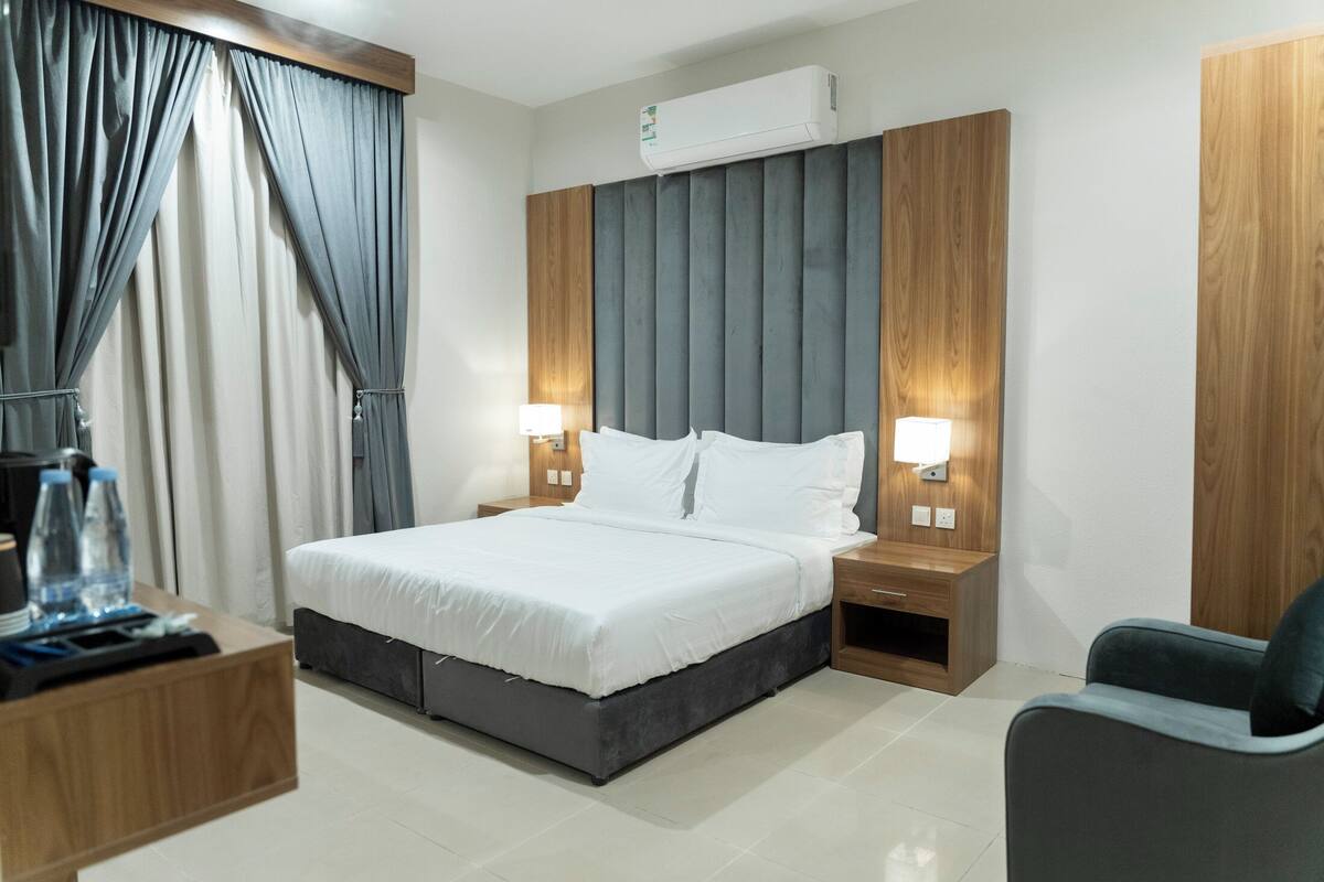 Habitación de hotel con cama, mesitas de noche, una silla, aire acondicionado y cortinas.