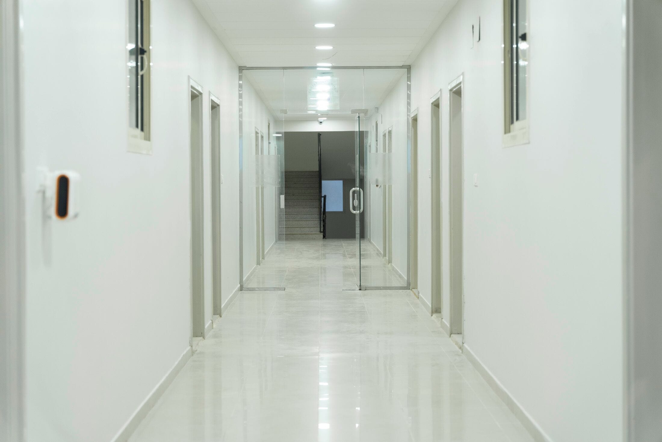 Un pasillo largo y estrecho con puertas de cristal a ambos lados, que conduce a una escalera.