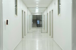 Um corredor comprido e estreito com portas de vidro em ambos os lados, que dá acesso a uma escadaria.