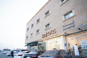 Um edifício com uma placa em árabe, várias janelas e carros estacionados na frente.
