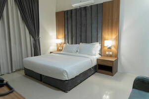 Una habitación de hotel moderna con una cama grande, dos mesitas de noche con lámparas, un cabecero de madera y una cortina gris.