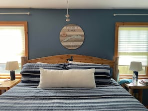 A bedroom with a wooden headboard, a bed with striped bedding, two bedside tables with lamps, and a wall-mounted sign indicating the room's location. - Camp Oliver Rose - Inlet's hidden gem (Inlet)