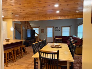 A wooden-floored dining area with a TV, wooden chairs, and a table. - Camp Oliver Rose - Inlet's hidden gem (Inlet)