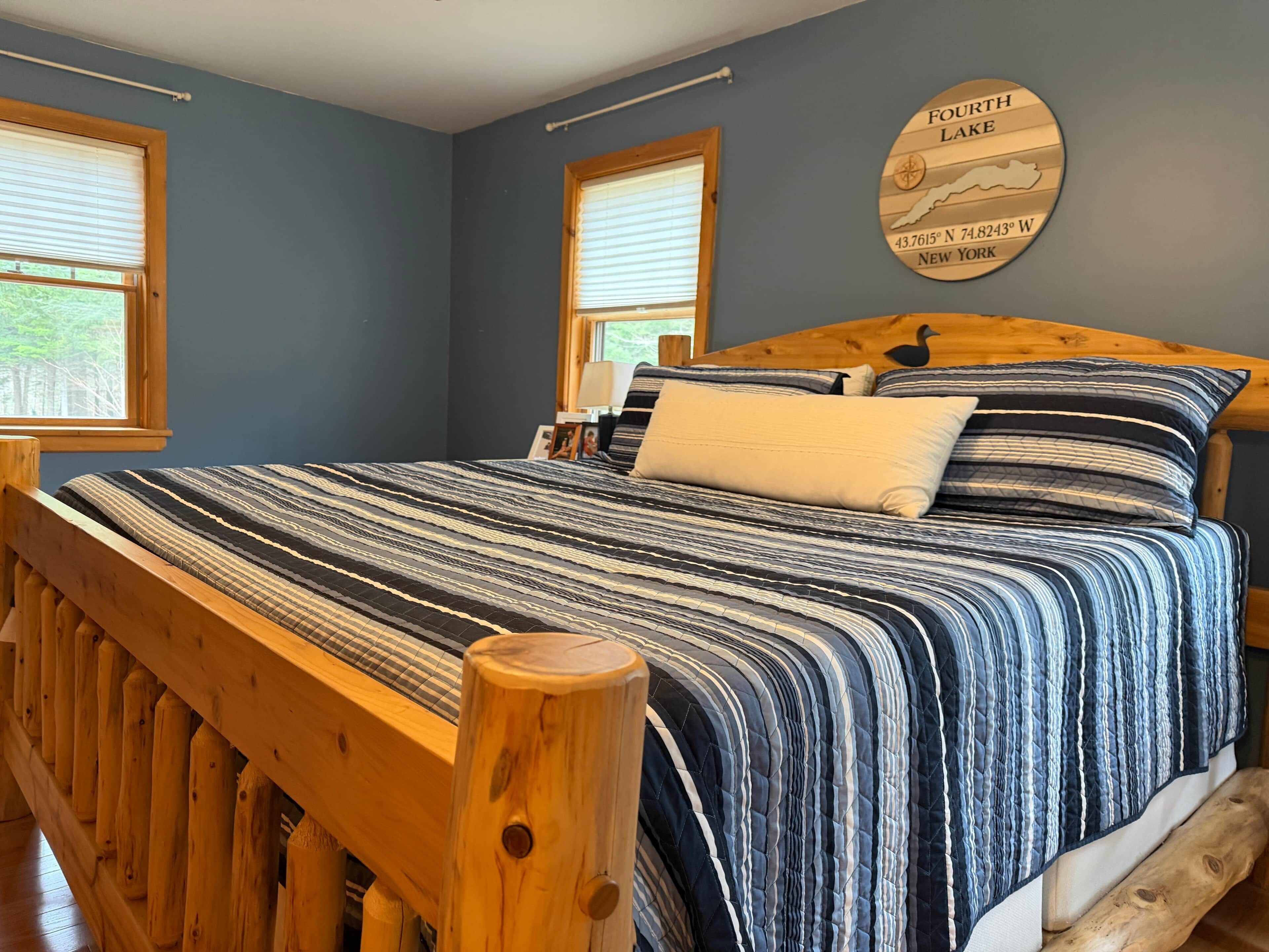 A bedroom with a wooden bed frame, a striped bedspread, and a wall clock.