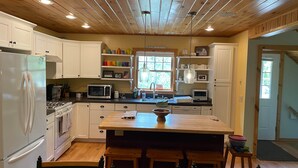 Una cocina con armarios blancos, techo de madera, una isla central con taburetes y un ventanal con vistas.