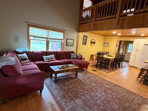 A living room with a red sofa, a coffee table, and a dining area with a wooden table and chairs. - Camp Oliver Rose - Inlet's hidden gem (Inlet)