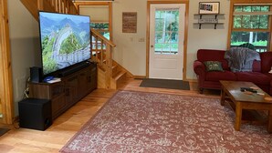 Sala de estar con televisor, escalera de madera, sofá rojo y puerta con vistas a la vegetación.