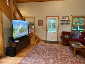 Sala de estar con televisor, escalera de madera, sofá rojo y puerta con vistas a la vegetación.
