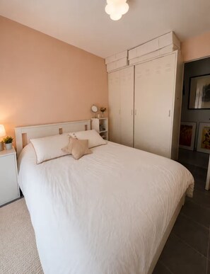 Ein Schlafzimmer mit einem Bett, Nachttischen, einem Kleiderschrank und einer Wandlampe.
