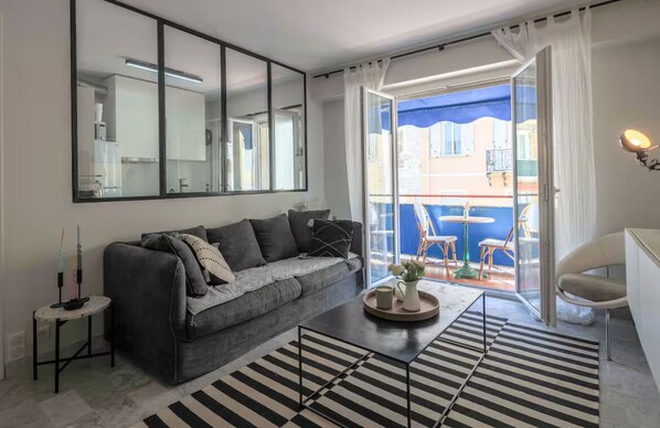 Ein modernes Wohnzimmer mit Sofa, Couchtisch, Beistelltisch, einem großen Spiegel und Blick auf den Balkon.