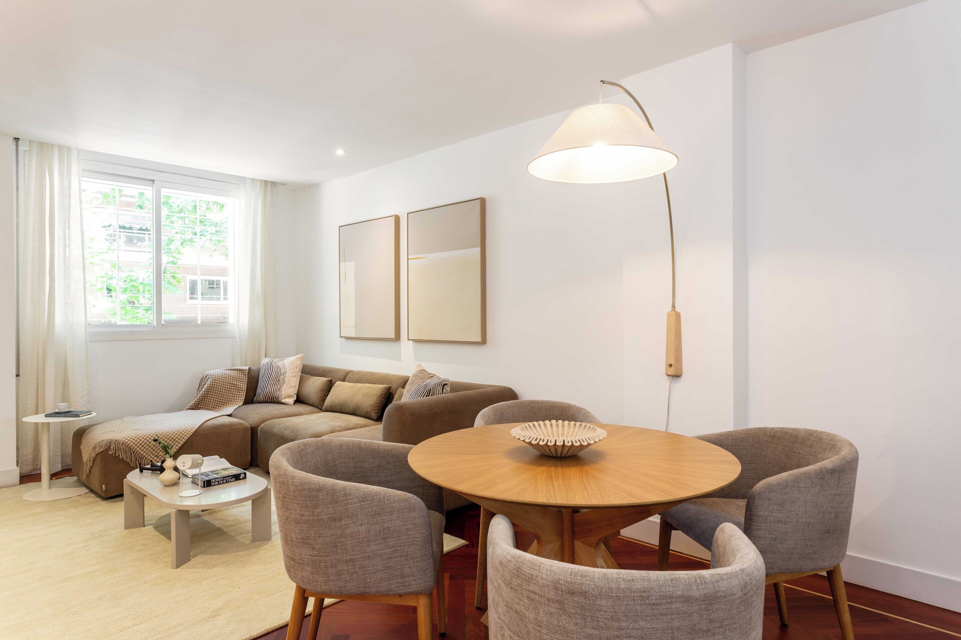 Een moderne woonkamer met een bank, een ronde eettafel en stoelen, een lamp en kunst aan de muur.