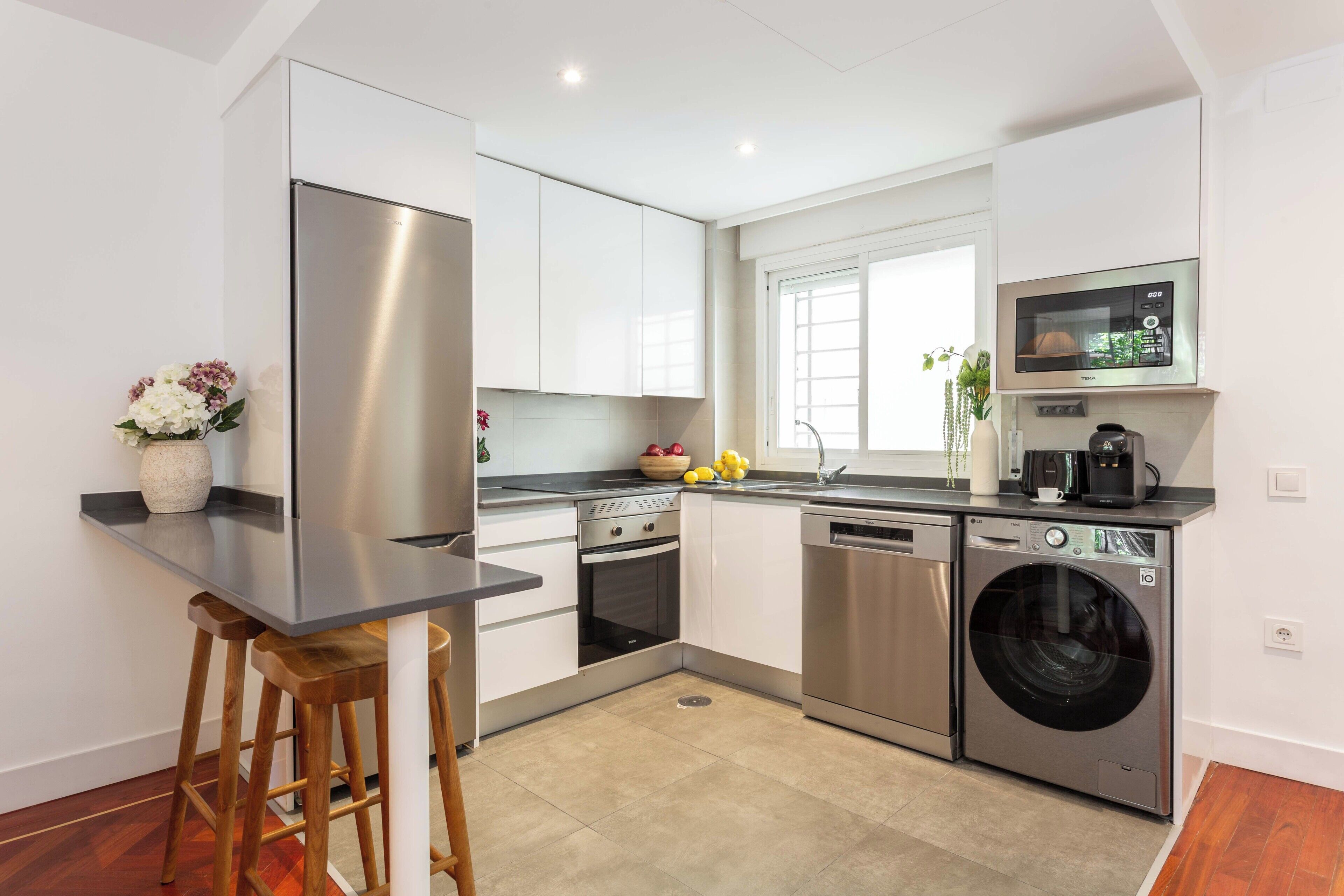 A modern kitchen with a stainless steel refrigerator, built-in oven, dishwasher, and washing machine.