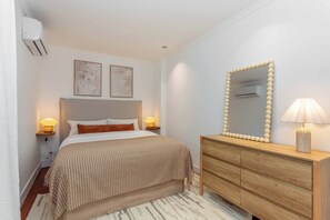 A bedroom with a bed, bedside lamps, a dresser, a mirror, and wall-mounted air conditioning. - This one-bedroom apartment at Calle Doctor Fleming 45, just steps from Plaza Castilla, combines contemporary design, comfort, and functionality in a space ideal for extended stays. (MADRID)