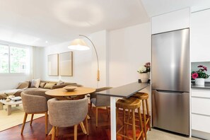 A modern kitchen with a stainless steel refrigerator, a dining area with a round table and chairs, and a bar stool. - This one-bedroom apartment at Calle Doctor Fleming 45, just steps from Plaza Castilla, combines contemporary design, comfort, and functionality in a space ideal for extended stays. (MADRID)