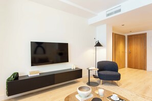 A modern living room with a flat-screen TV, a dark sofa, a small side table, a floor lamp, and a wooden door. - This apartment with a separate bedroom at Calle Doctor Fleming 45, next to Plaza Castilla, combines elegance, comfort, and functionality in a space ideal for extended stays. (MADRID)