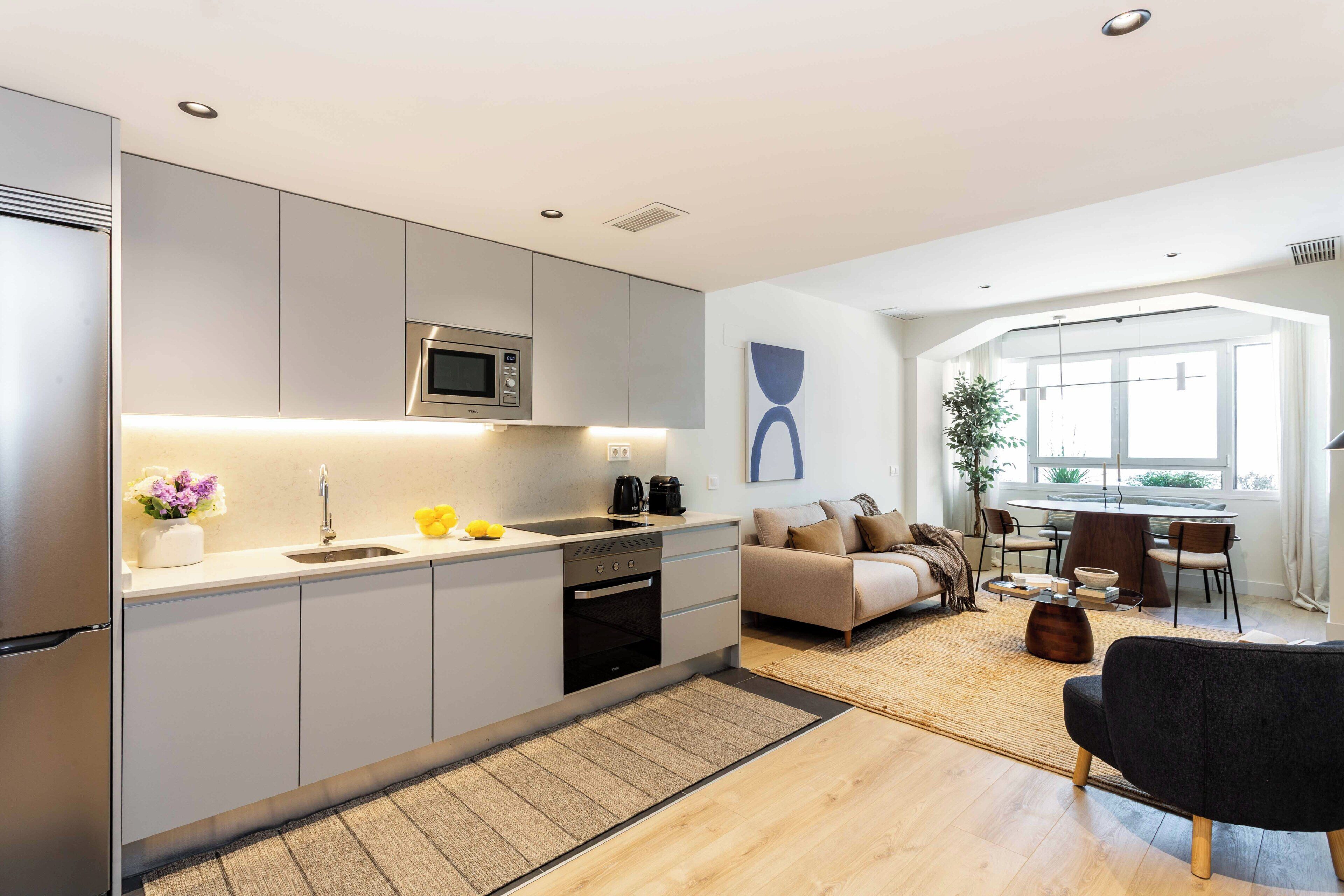 A modern kitchen with built-in appliances, a dining area with a round table, and a living space with a sofa and a coffee table.