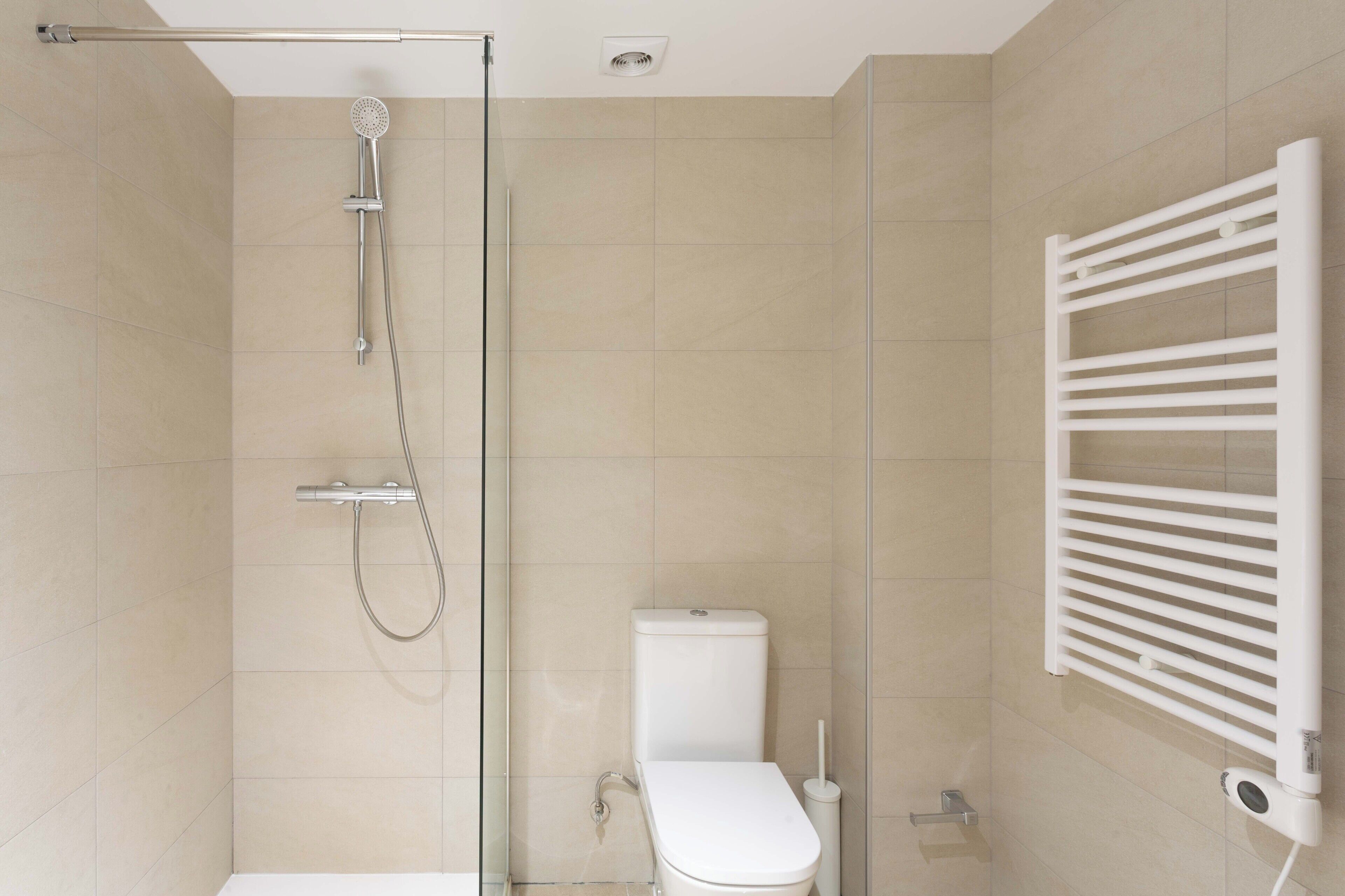A modern bathroom with a glass shower enclosure, a white toilet, and a wall-mounted towel rack.