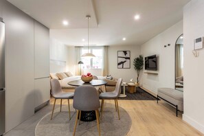 A modern living room with a dining area, a sofa set, a TV, and a plant. - This contemporary design studio apartment at Calle Doctor Fleming 45, next to Plaza Castilla, offers an elegant, functional, and welcoming accommodation experience, ideal for extended stays. (MADRID)
