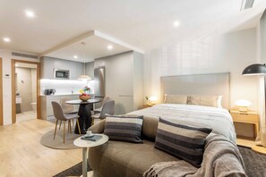 A modern hotel room with a bed, bedside table, lamp, and a small round table with chairs. - This contemporary design studio apartment at Calle Doctor Fleming 45, next to Plaza Castilla, offers an elegant, functional, and welcoming accommodation experience, ideal for extended stays. (MADRID)