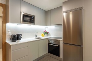 A modern kitchen with a built-in microwave, a coffee maker, a sink, and a stainless steel refrigerator. - This contemporary design studio apartment at Calle Doctor Fleming 45, next to Plaza Castilla, offers an elegant, functional, and welcoming accommodation experience, ideal for extended stays. (MADRID)
