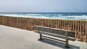 Un banc situé près d’une plage, avec une clôture en bois et une vue dégagée sur l’océan.