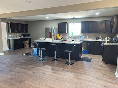 A modern kitchen with dark cabinetry, a central island with bar stools, a refrigerator, and a window providing natural light.. New Vrindaban guest house, 1 to 5 bedroom house with AC in cozy Moundsville