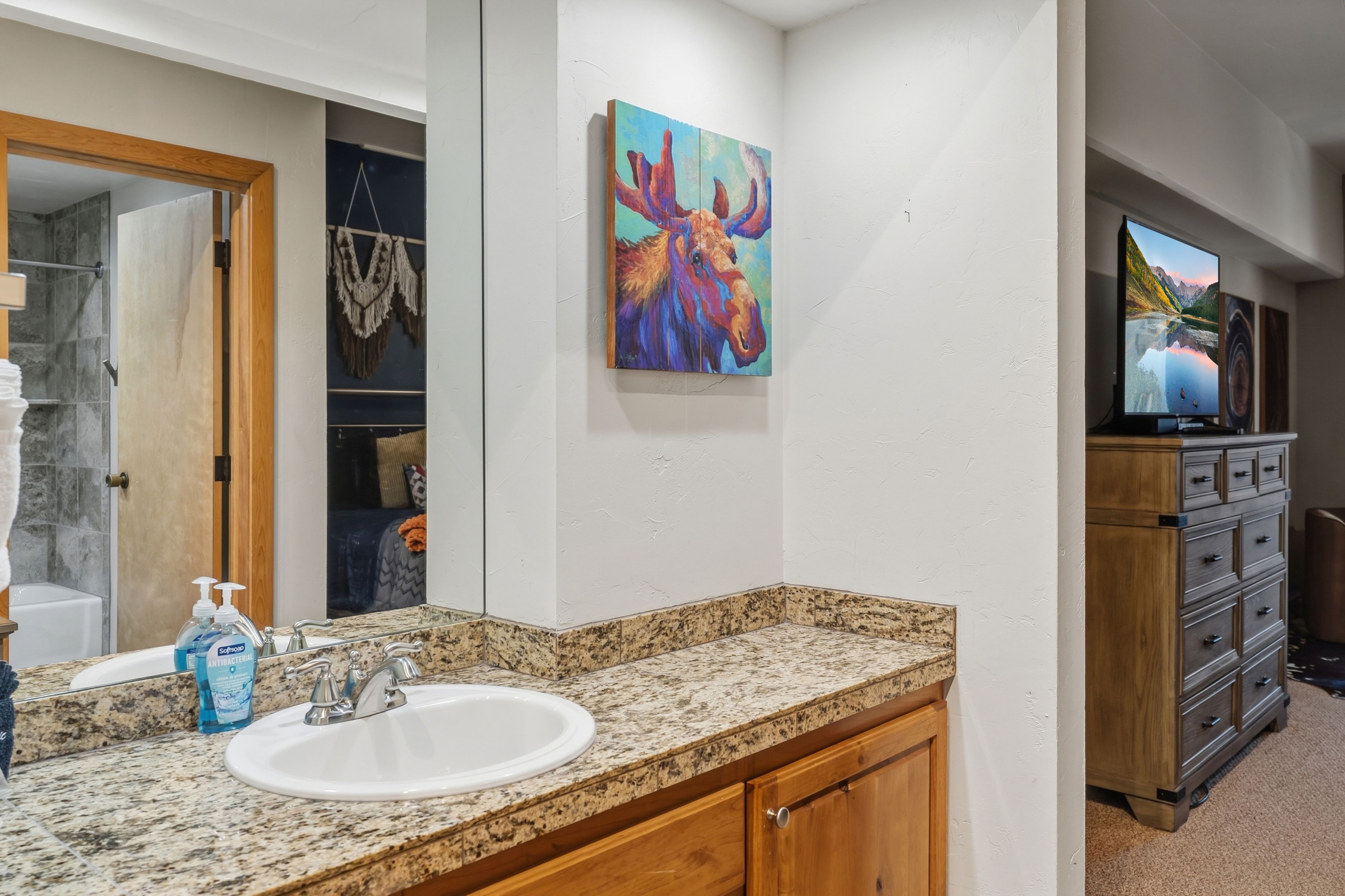 Un baño con encimera de granito, lavamanos blanco y mueble de madera.