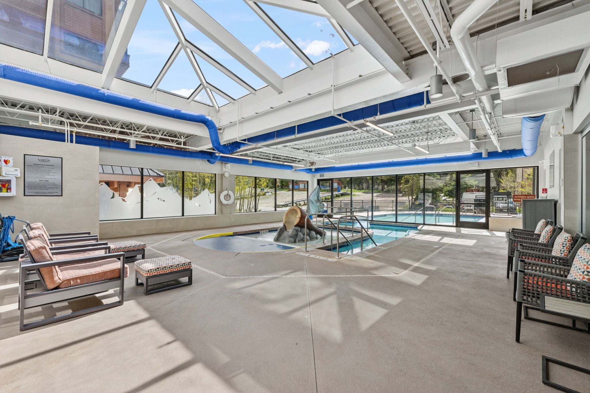 A pool area with lounge chairs, a glass ceiling, and a view of the outside.