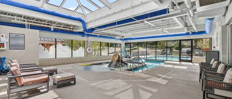 A pool area with lounge chairs, a glass ceiling, and a view of the outside.