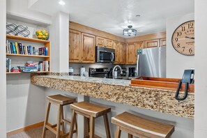 A kitchen with wooden cabinets, granite countertops, a stainless steel refrigerator, a microwave, and a clock on the wall. - Pool! Next to Lifts! (Breckenridge)