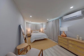 A modern hotel room with a large bed, a bedside table with a lamp, a dresser, and an air conditioning unit on the wall. - Coastal haven in prime location (Clearwater)