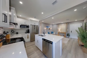 A modern kitchen with white cabinetry, stainless steel appliances, and a central island. - Coastal haven in prime location (Clearwater)