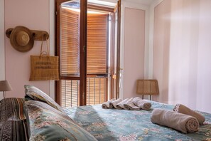 Ein Schlafzimmer mit einem Bett, einer Holztür mit Rollläden, einem gewebten Korb und einem Hut an der Wand.