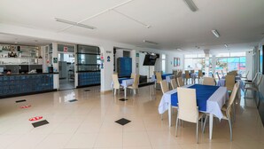 Un comedor limpio y bien iluminado con mesas y sillas, una recepción y una cocina al fondo.
