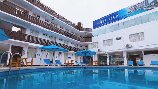 Un hotel con piscina, varios balcones y sombrillas azules.