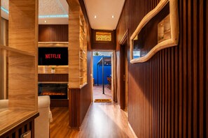 Un couloir aux murs recouverts de boiseries, un panneau indiquant la présence de Netflix et une cheminée.