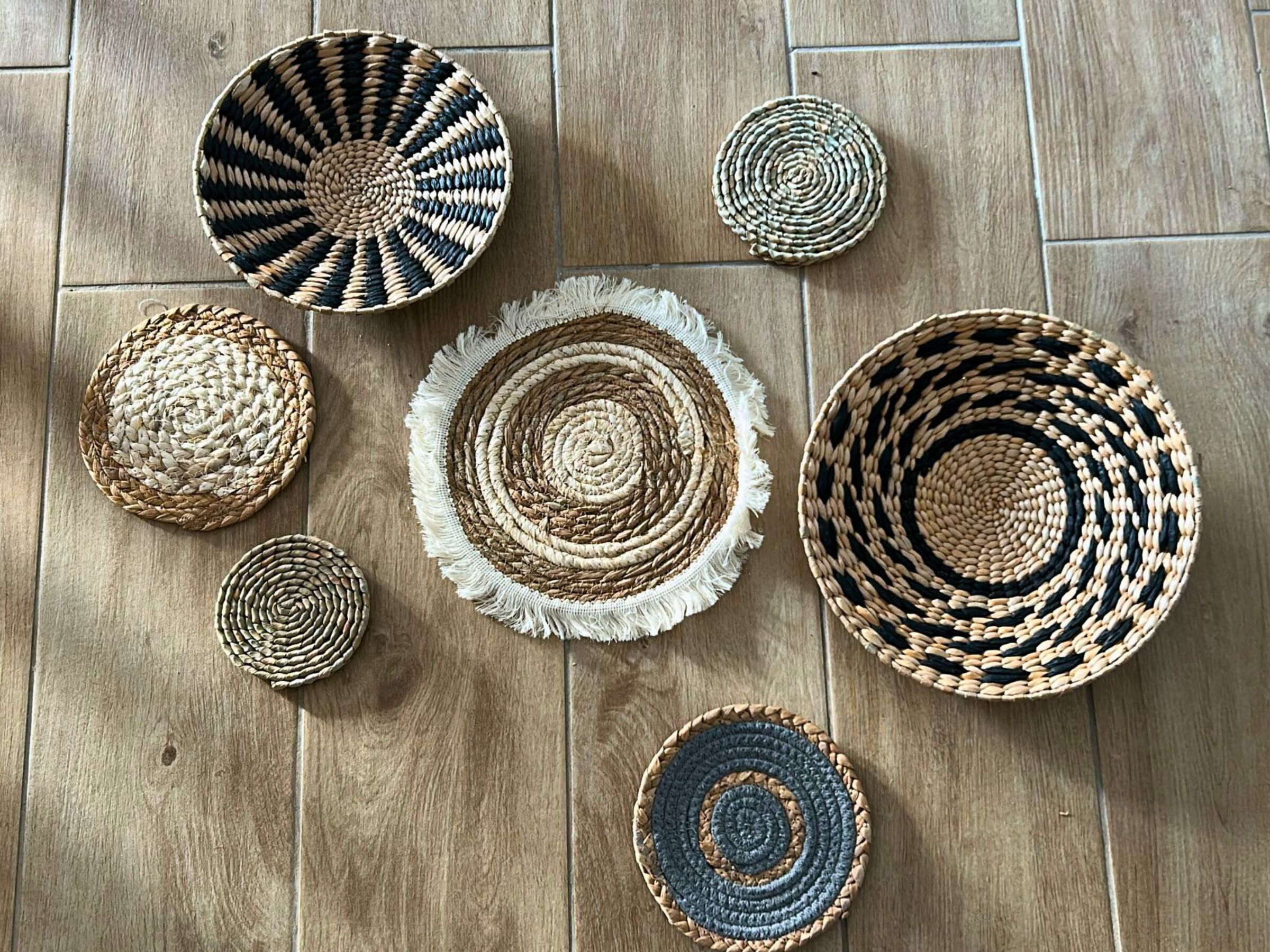 A variety of woven coasters arranged on a wooden floor.