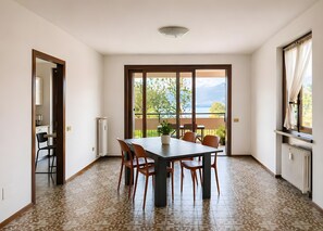 Un comedor con una mesa y sillas, un radiador, un ventanal con cortinas y vistas a un balcón con mobiliario exterior.