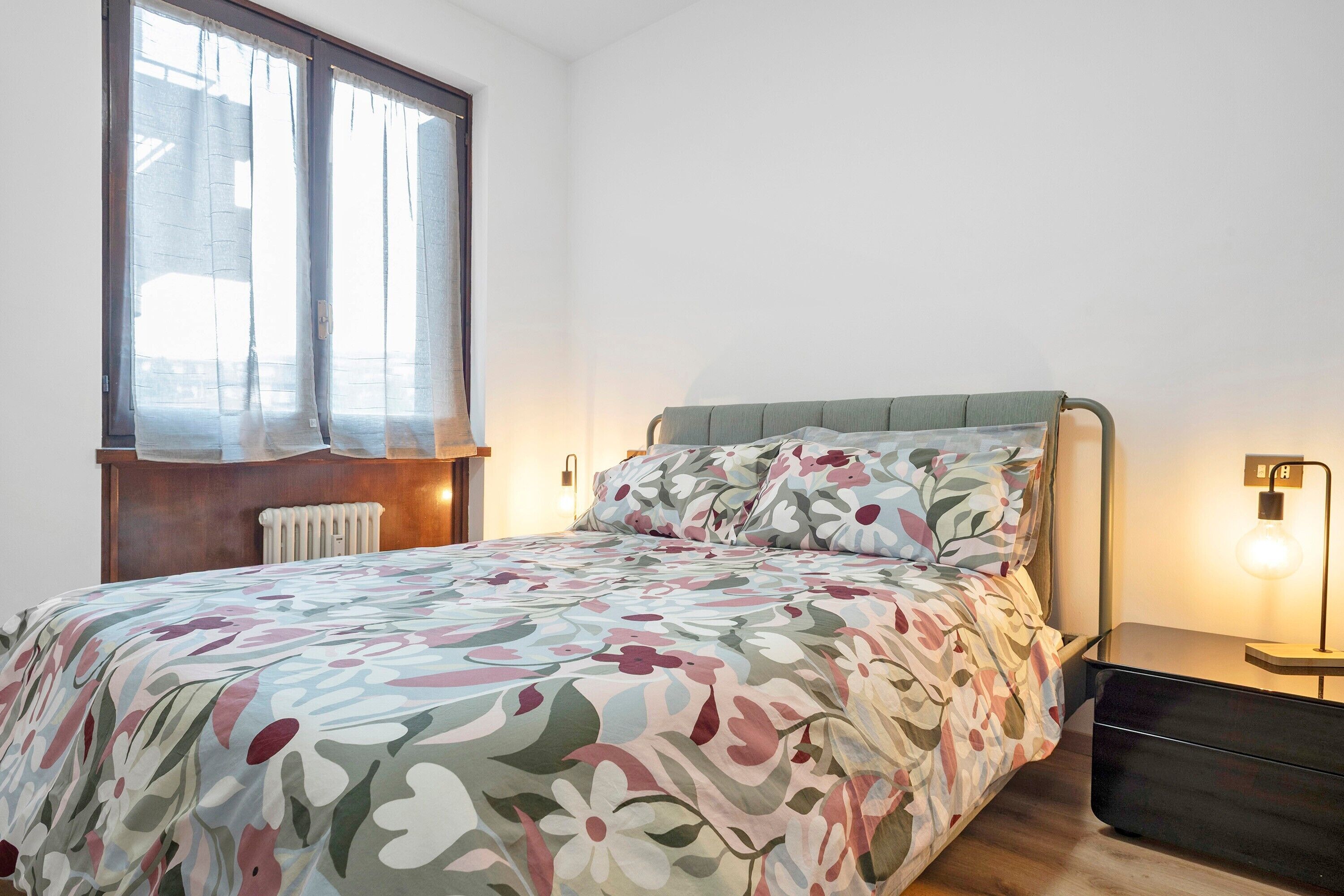 Une chambre à coucher avec un lit, un radiateur, une fenêtre avec des rideaux et une lampe de chevet.