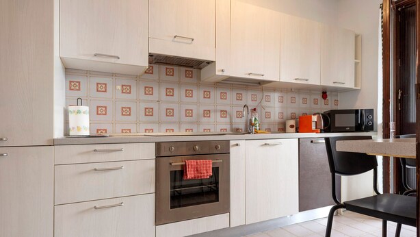 Une cuisine moderne avec des meubles de couleur bois clair, un four en acier inoxydable, un four à micro-ondes et une machine à café posée sur le plan de travail.
