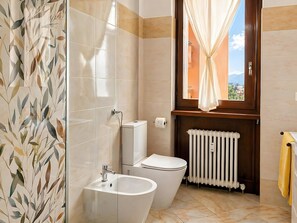 Un baño con inodoro, bidé y una ventana con cortinas.
