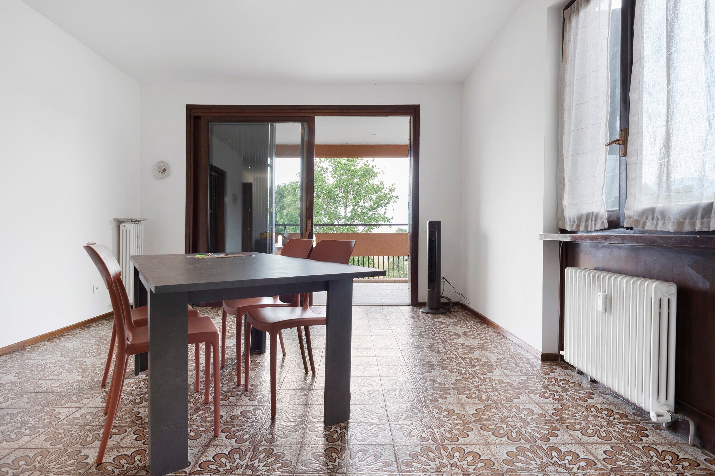 Un coin repas avec une table et des chaises, un radiateur et une vue sur l’extérieur, accessible par une porte coulissante.