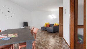 Une pièce comprenant une table à manger, des chaises, un canapé avec des coussins, un téléviseur et une horloge murale.