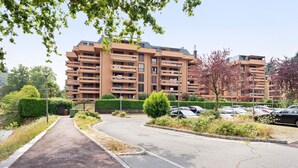 Un immeuble résidentiel à plusieurs étages, doté de balcons, d’un parking et d’un chemin menant à l’entrée.