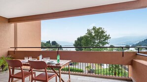 Un balcon avec une table dressée pour deux personnes, offrant une vue panoramique sur un lac et des montagnes.