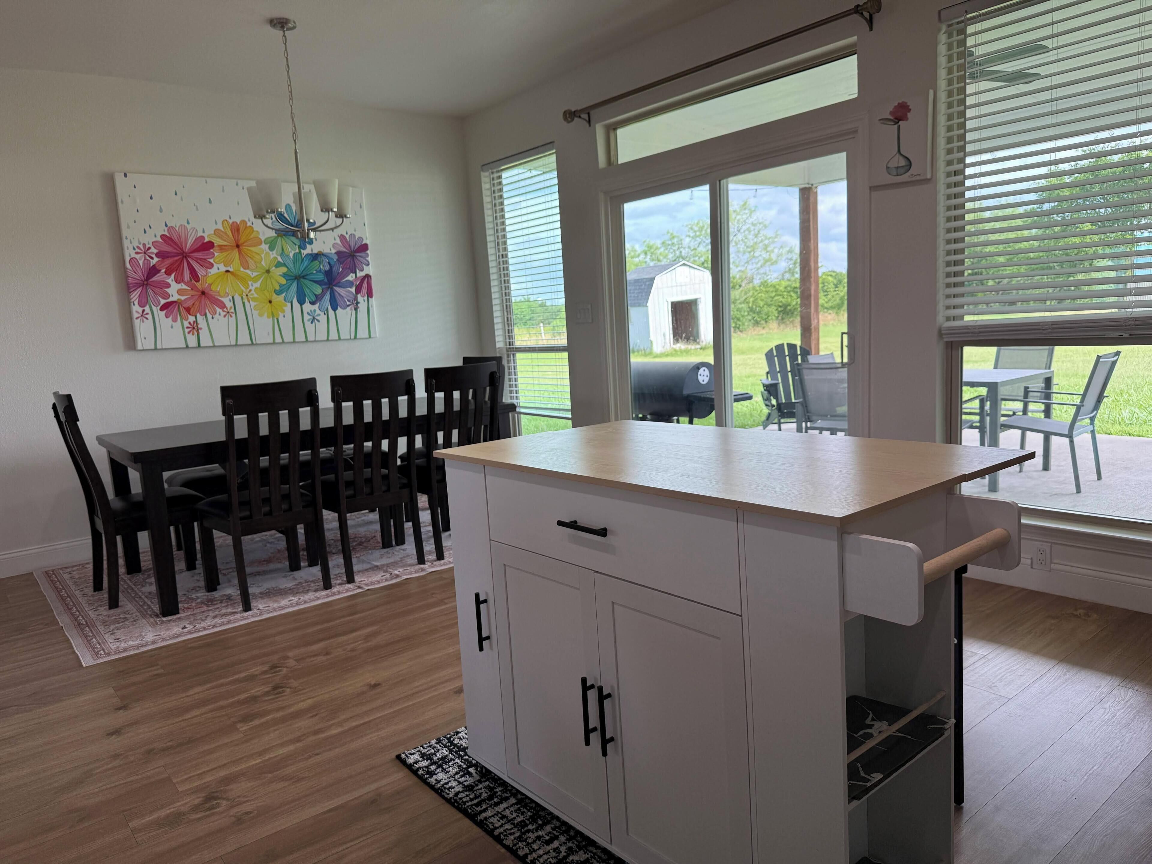 A modern kitchen with a dining area, large windows, and a view of the outdoors.